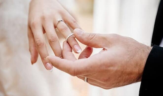 groom puts wedding ring on brides left hand